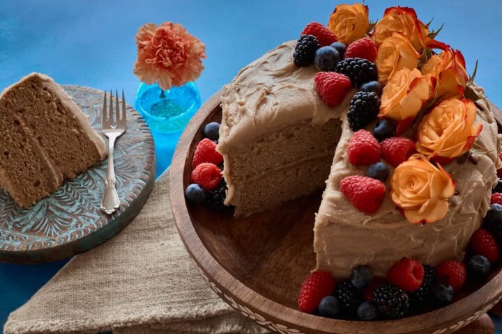 the finished dessert decorated with flowers and berries on a plate, with one slice removed and placed on a separate plate