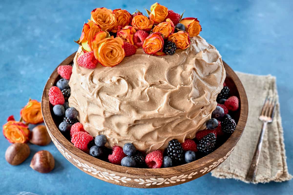 cake decorated with flowers and berries on a cake stand with chestnuts, flowers, a napkin, and a fork in the foreground