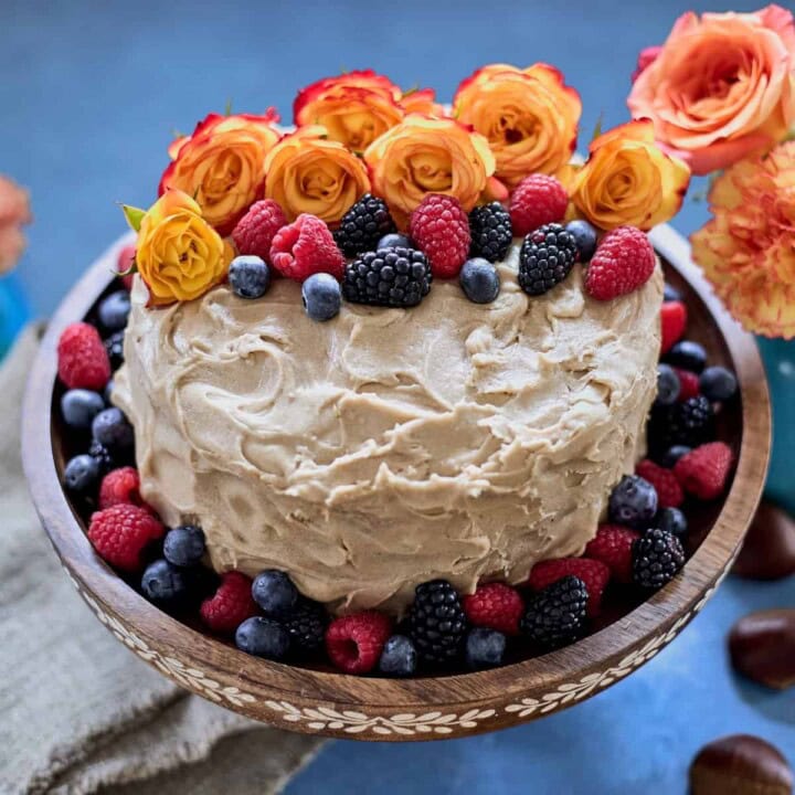 a cake, decorated with flowers and berries, on a stand