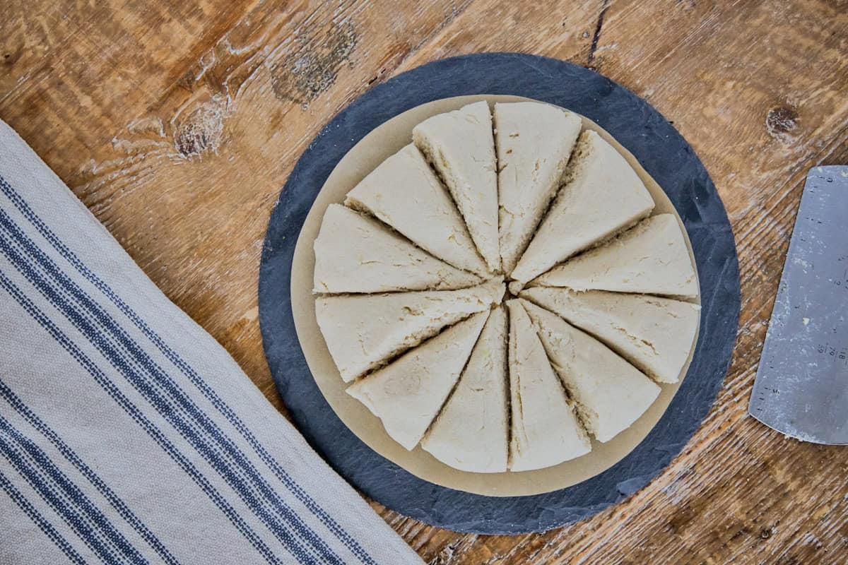 a circle of tortilla dough divided into pie-shaped sections with a bench scraper and a kitchen towel alongside