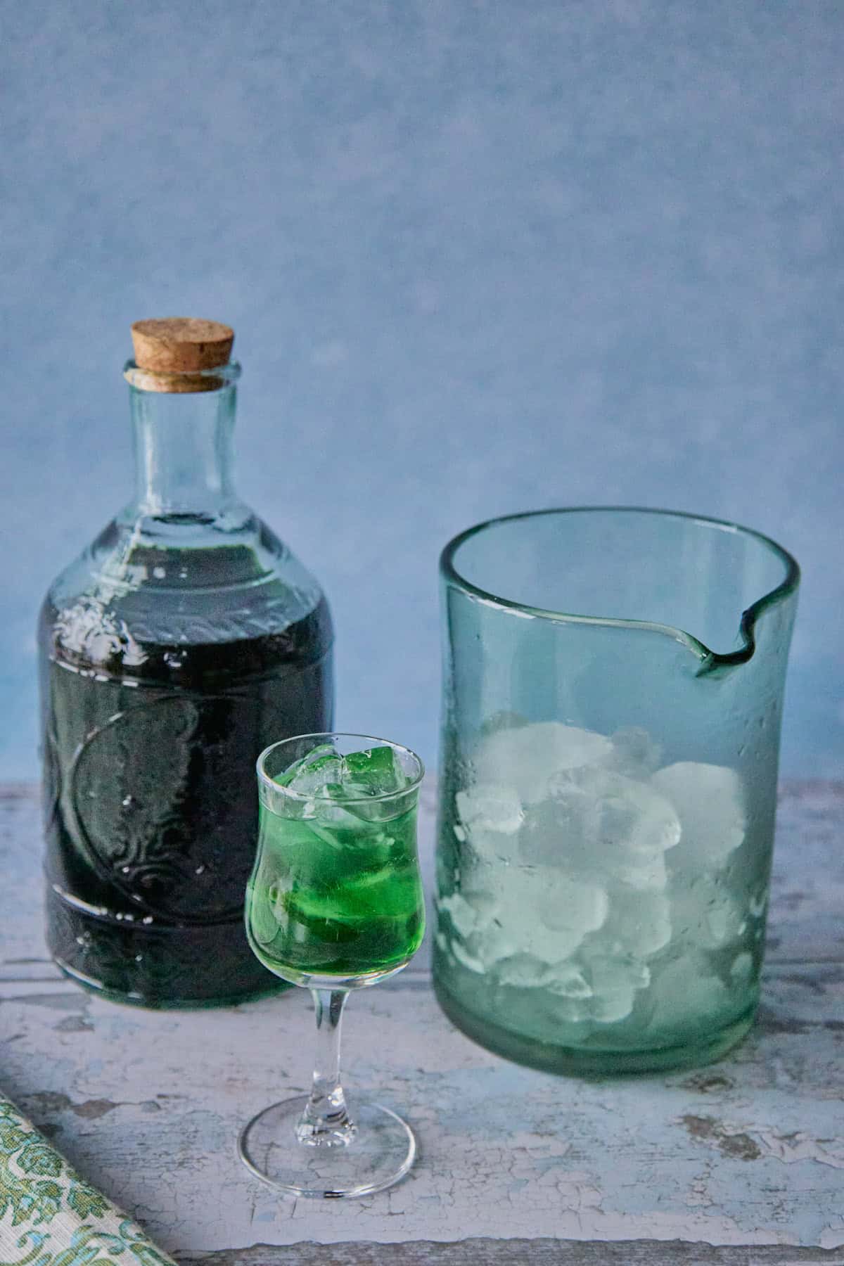 a bottle of liqueur, a mixing glass with ice, and a small glass full of liqueur and ice, with a napkin in the foreground
