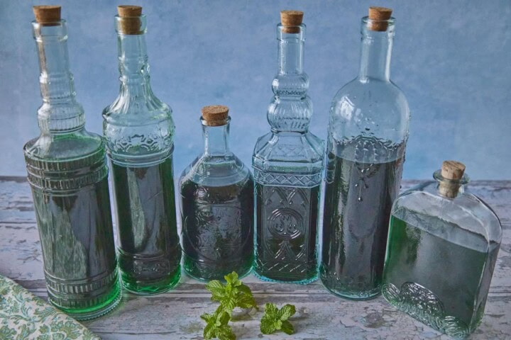 6 bottles of liqueur with a napkin and some fresh sprigs of mint in the foreground