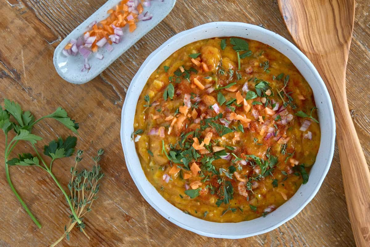 finished sauce in a bowl with garnishes and a wooden cooking spoon in the background