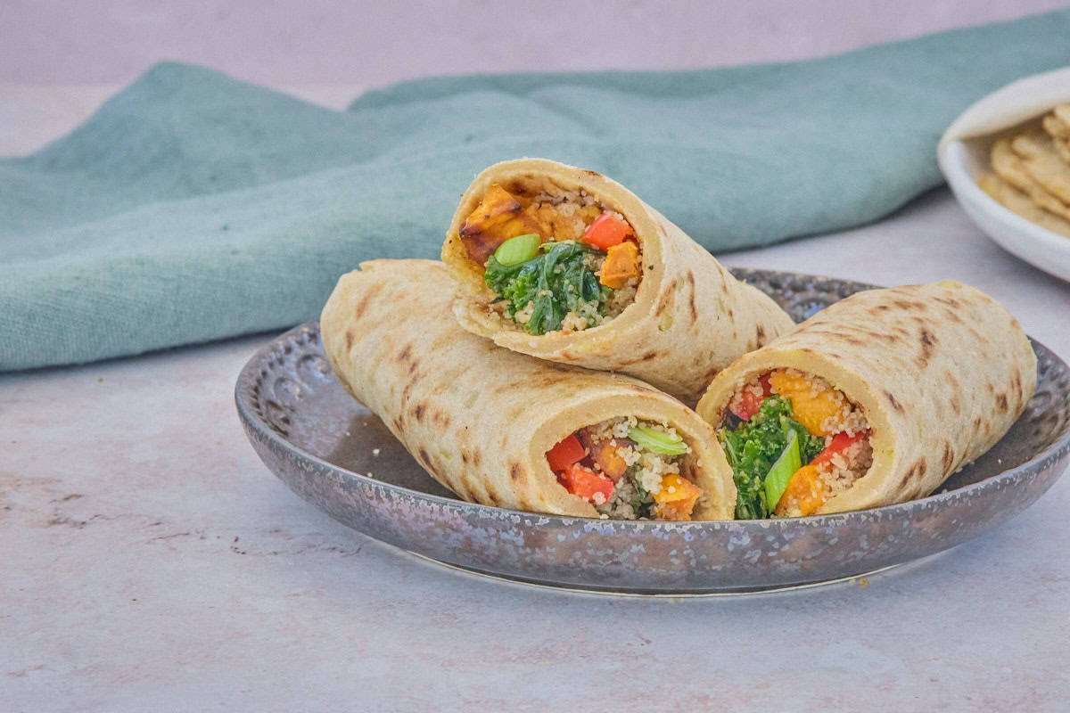 filled wraps on a plate with a napkin and stack of tortillas on a plate in the background