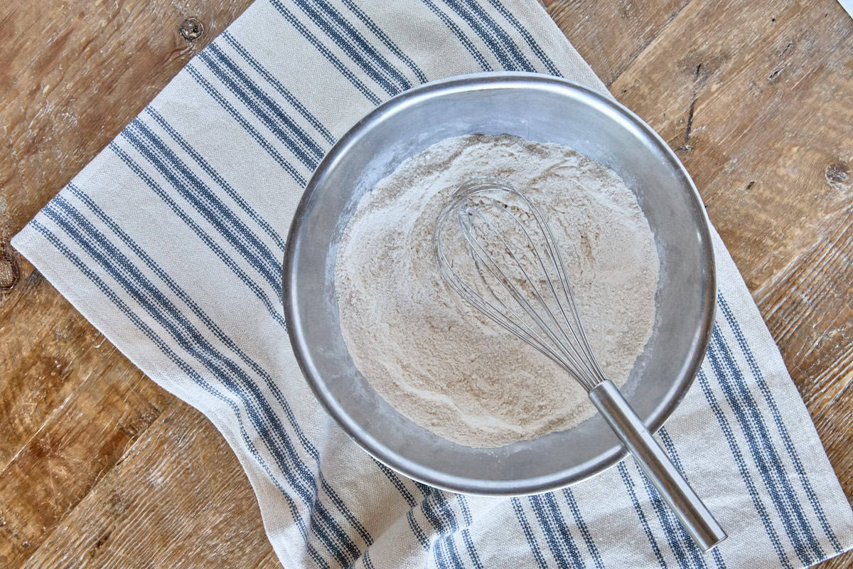 a whisk in a bowl of dry dough ingredients, with a kitchen towel beneath