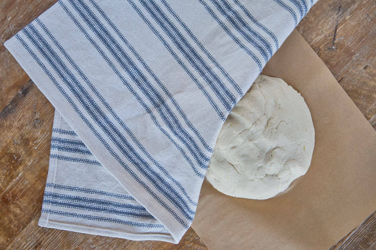 a circle of dough atop a sheet of parchment paper with a kitchen towel folded and partially draped over the top