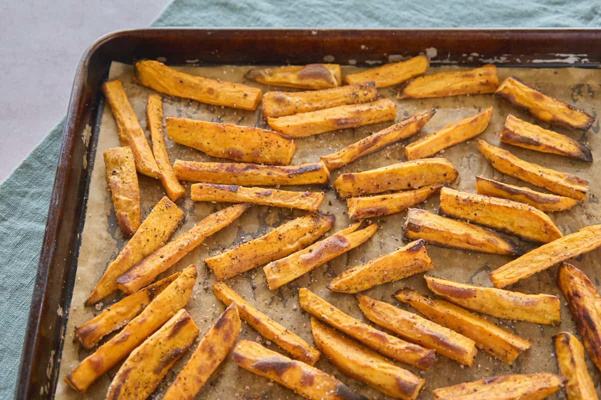 roasted strips of sweet potatoes on a sheet of parchment paper on a baking sheet, with a napkin beneath