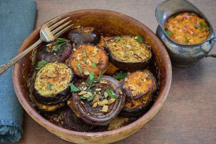 roasted veggies in a rustic dish with a fork and napkin, and a small pitcher of sauce on the side