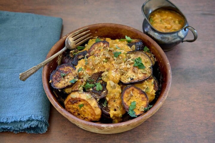 roasted veggies in a rustic dish with a fork and napkin, sauce in a small pitcher on the side, and sauce drizzled over the veggies