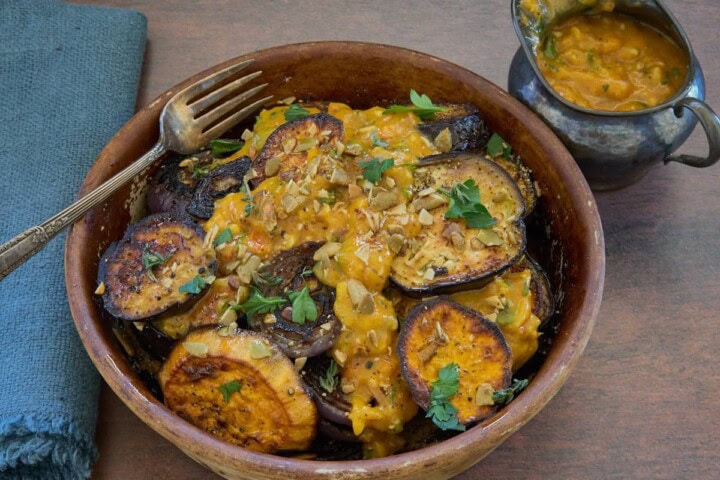 close-up shot of roasted veggies in a dish with sauce drizzled on top with a fork and napkin and small pitcher of sauce on the side