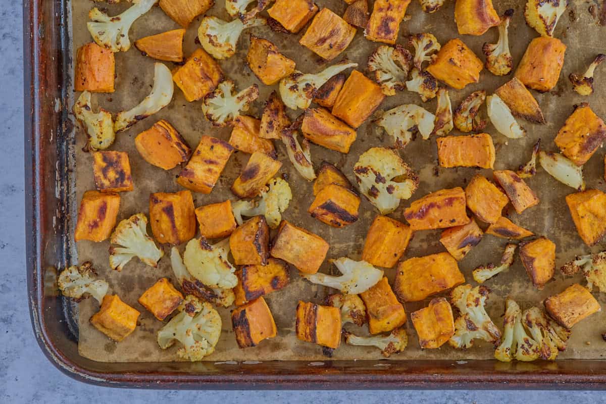 roasted chunks of sweet potatoes and cauliflower florets on a sheet of parchment paper on a baking sheet