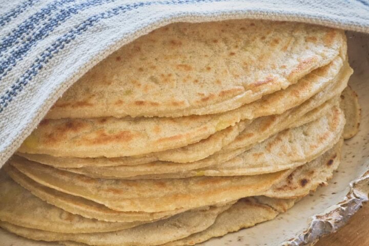 stack of tortillas on a plate with a kitchen towel draped diagonally over the top