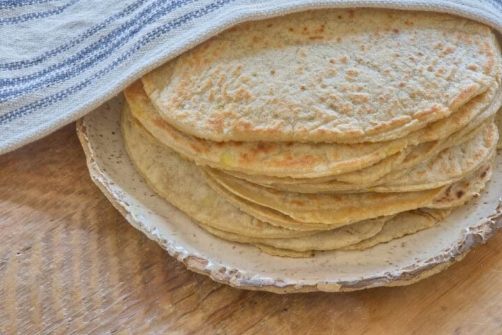 a stack of tortillas on a plate offset to the side with a kitchen towel draped over the top