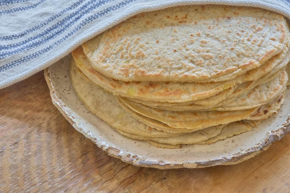 a stack of tortillas on a plate offset to the side with a kitchen towel draped over the top