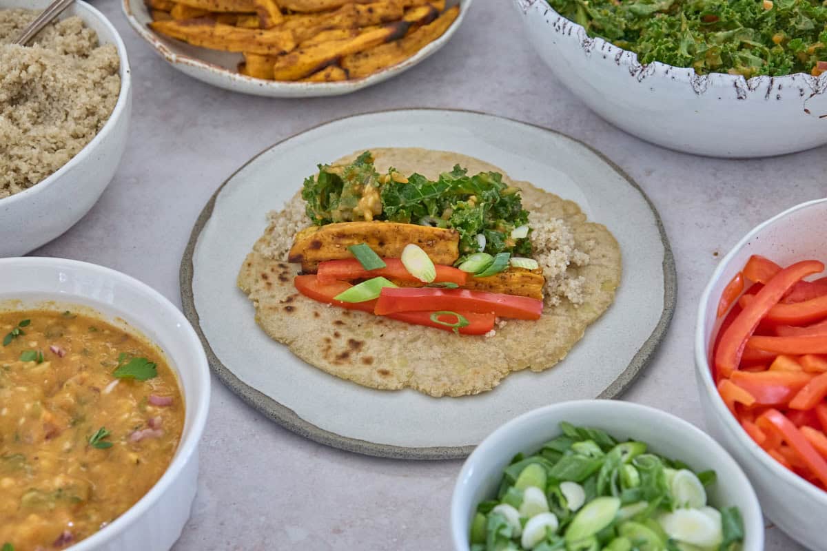 a tortilla on a plate in the center, topped with wrap ingredients, with ingredients in separate bowls in a circle around this plate