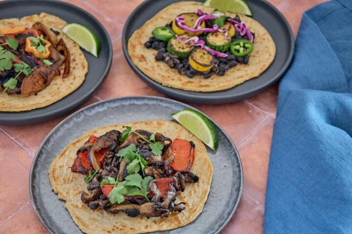 three plates with tortillas topped with veggies, and a napkin alongside