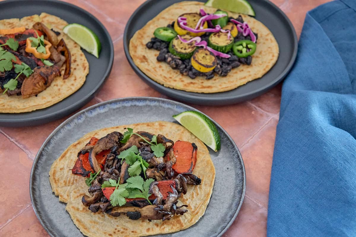 three plates with tortillas topped with veggies, and a napkin alongside