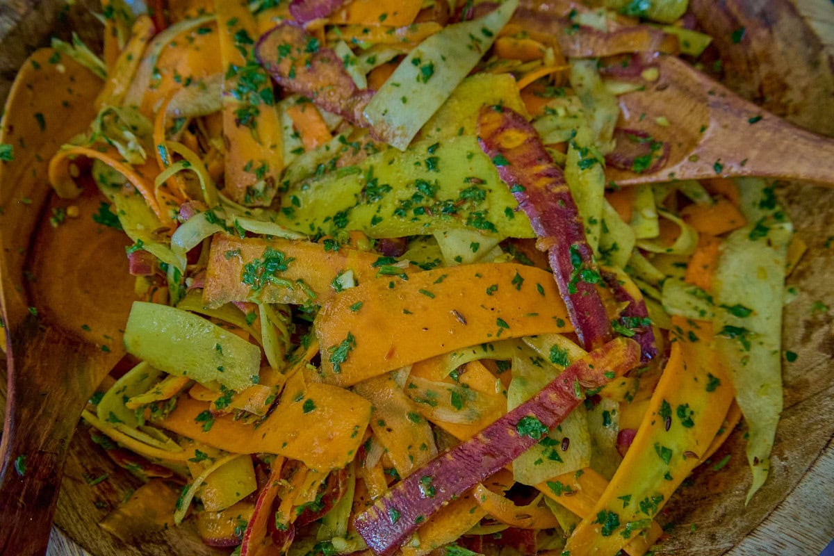 a close-up shot of carrot ribbons in chermoula sauce in a large wooden bowl with 2 wooden salad serving spoons