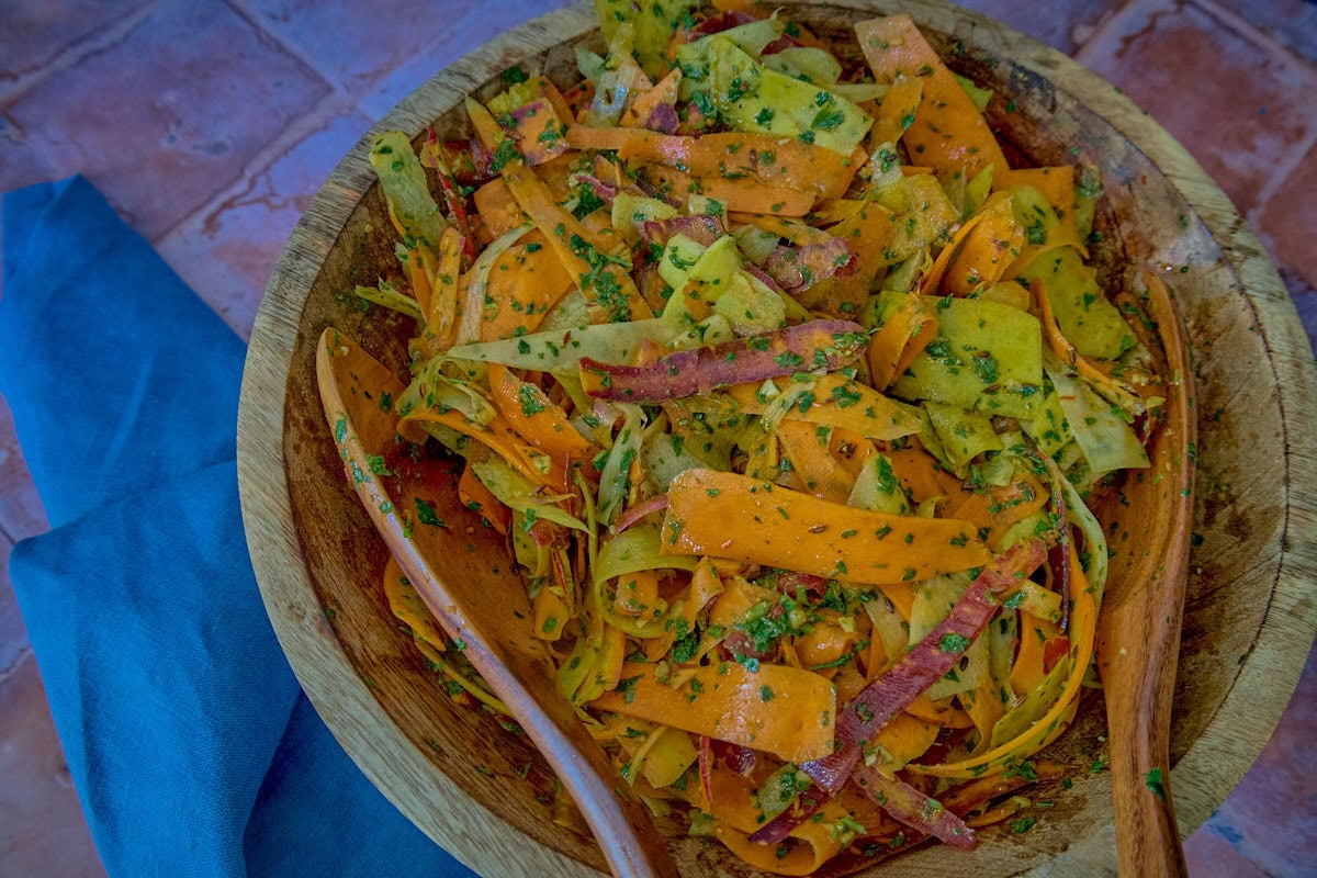 carrot ribbons in chermoula sauce in a large wooden bowl with 2 wooden salad serving spoons and a napkin