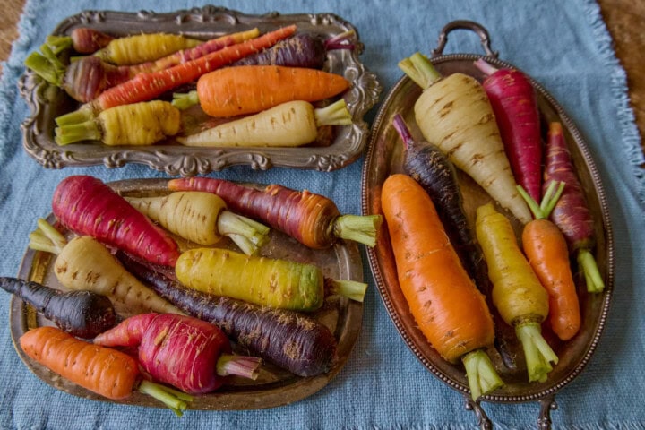 various colored carrots on 3 small vintage metal trays on a napkin