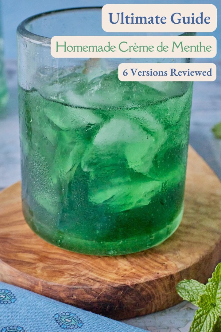 a glass with ice and crème de menthe liqueur on a round wooden board with a napkin and sprig of mint in the foreground