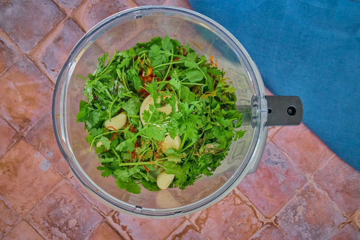 unblended ingredients for chermoula sauce in a food processor, with a napkin alongside