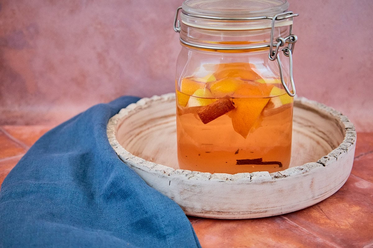 alcohol, citrus zest, sugar, and spices mixed in a sealed jar on a tray for version 1 of the vin d'orange, with a napkin in the background