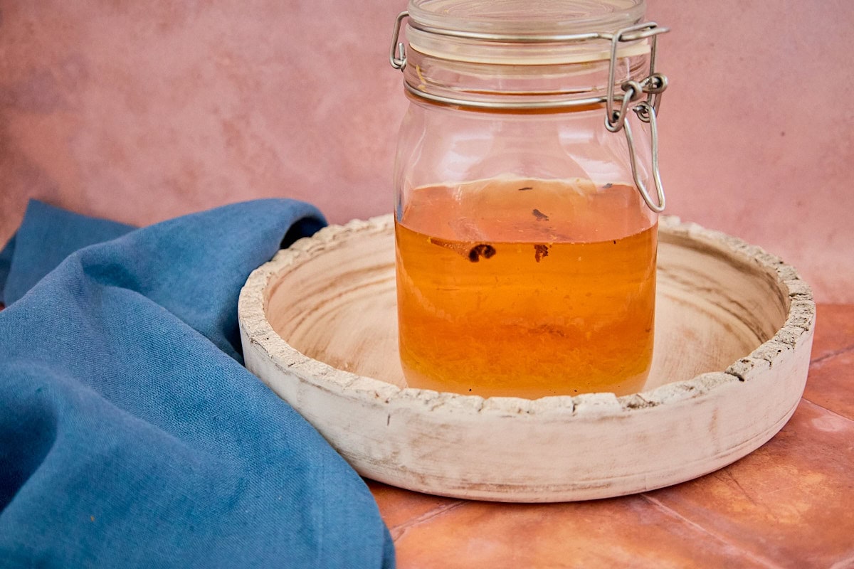 alcohol, citrus zest, sugar, and spices mixed in a sealed jar on a tray for version 3 of the vin d'orange, with a napkin in the background