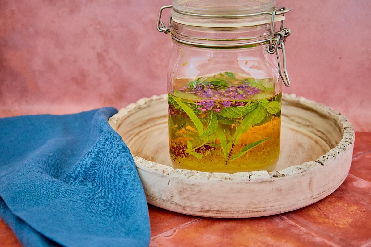 fresh herbs, alcohol, citrus zest, sugar, and spices mixed in a sealed jar on a tray for version 4 of the vin d'orange, with a napkin in the background