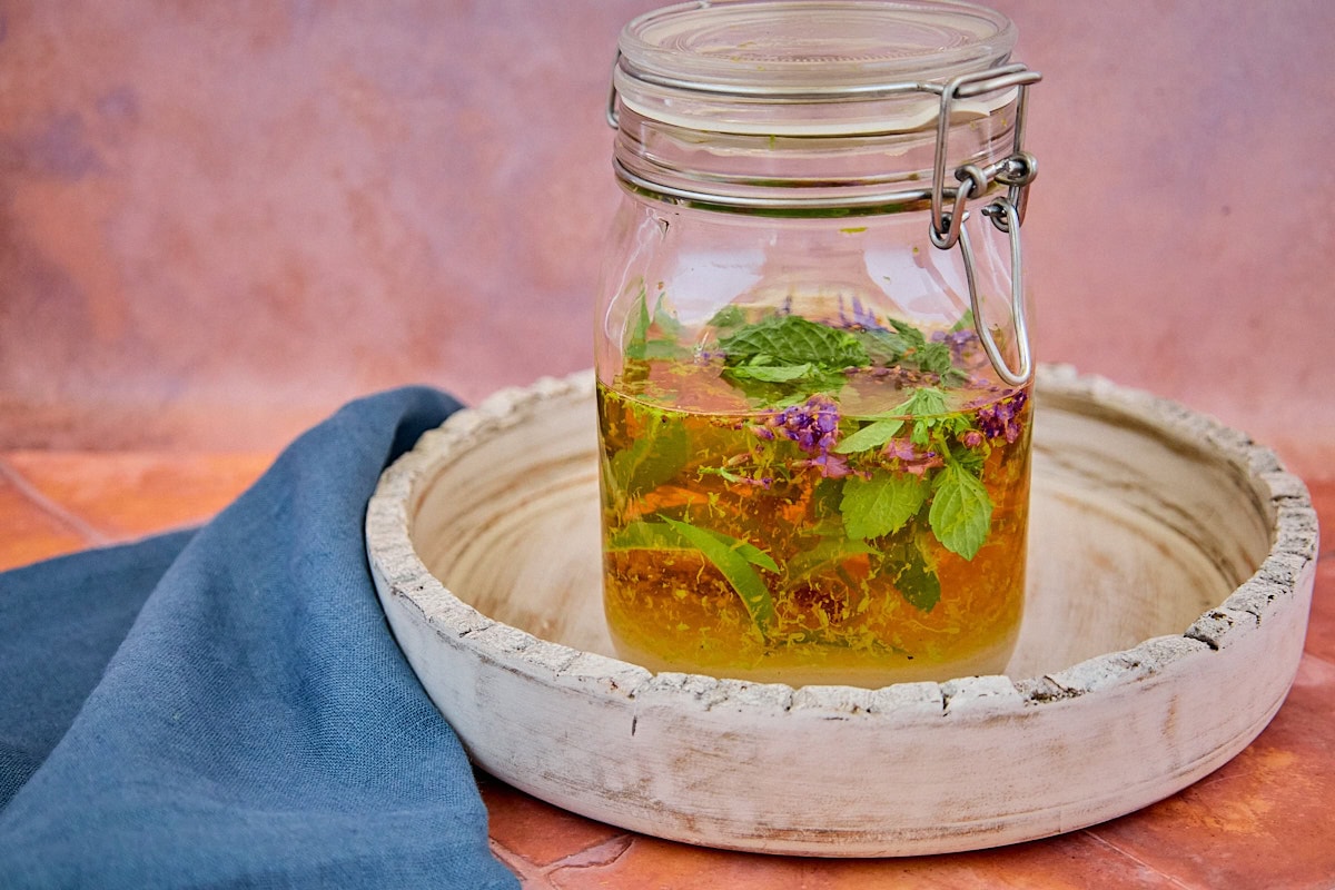fresh herbs, alcohol, citrus zest, sugar, and spices mixed in a sealed jar on a tray for version 5 of the vin d'orange, with a napkin in the background