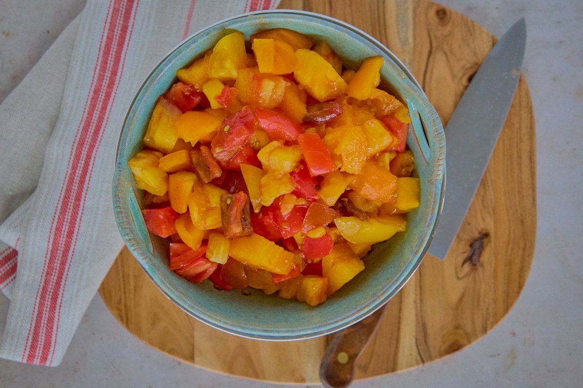 a bowl of diced tomatoes on a wooden board with a kitchen towel and a chef's knife alongside