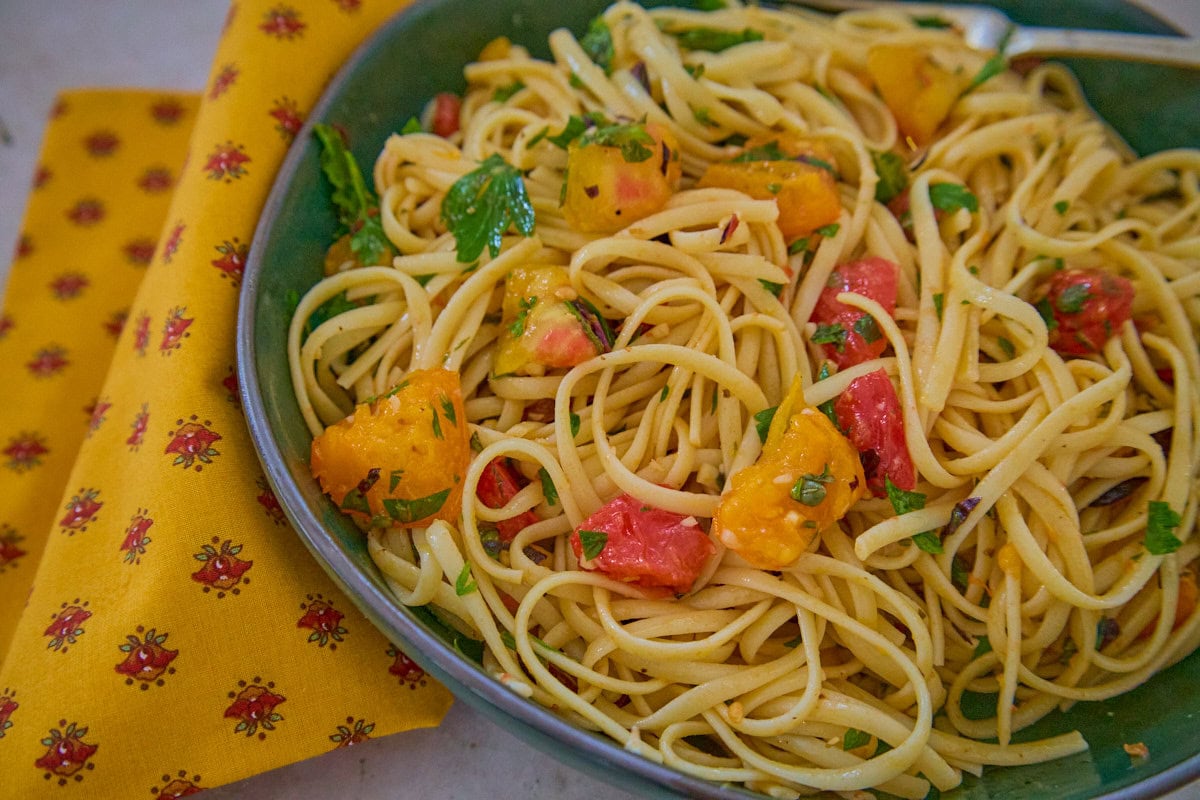an offset close-up of a green bowl of pasta and sauce with a fork, and a napkin alongside