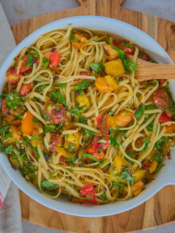 a bowl of pasta and sauce with a wooden spoon on a wooden board with a kitchen towel alongside