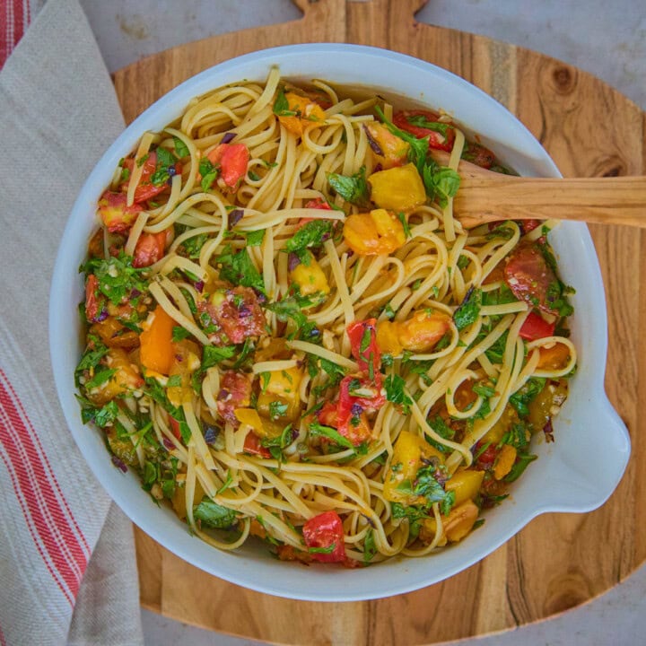 a bowl of pasta and sauce with a wooden spoon on a wooden board with a kitchen towel alongside