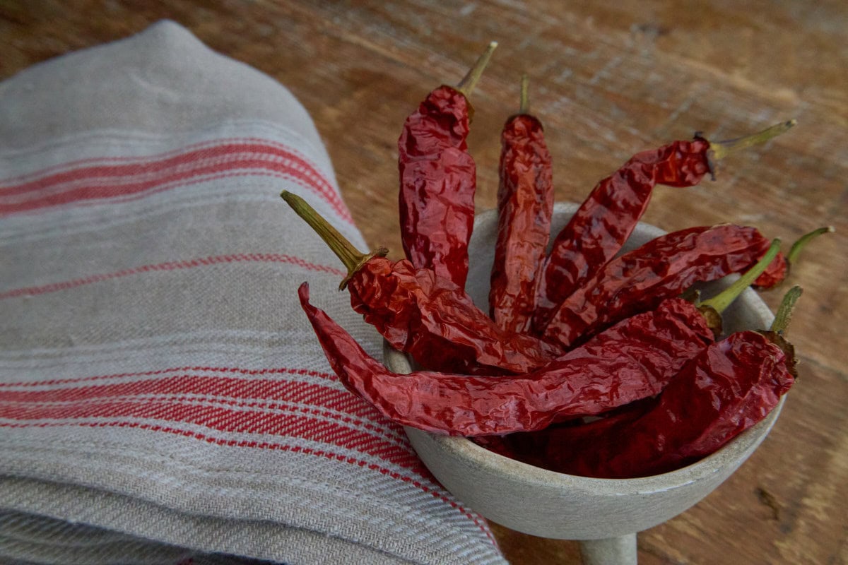 dried buena mulata peppers in a footed bowl with a kitchen towel alongside