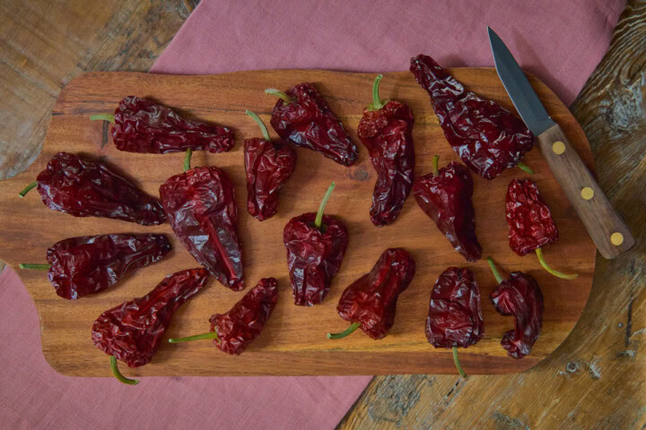 dried leutschauer paprika peppers on a wooden cutting board with a paring knife atop a napkin on a rustic wood table