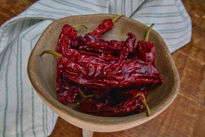 dried pasilla bajio chilaca peppers in a bowl with a kitchen towel in the background
