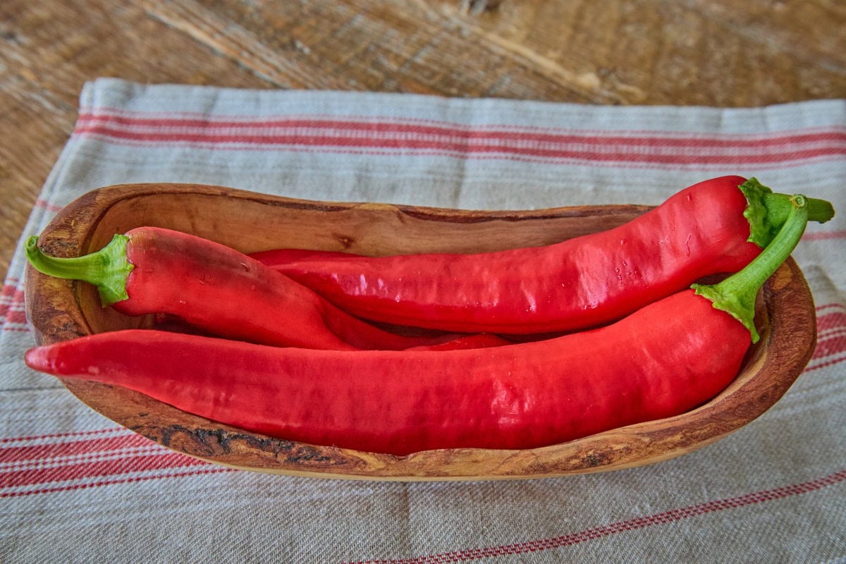 fresh numex big jim peppers in a wooden bowl atop a kitchen towel