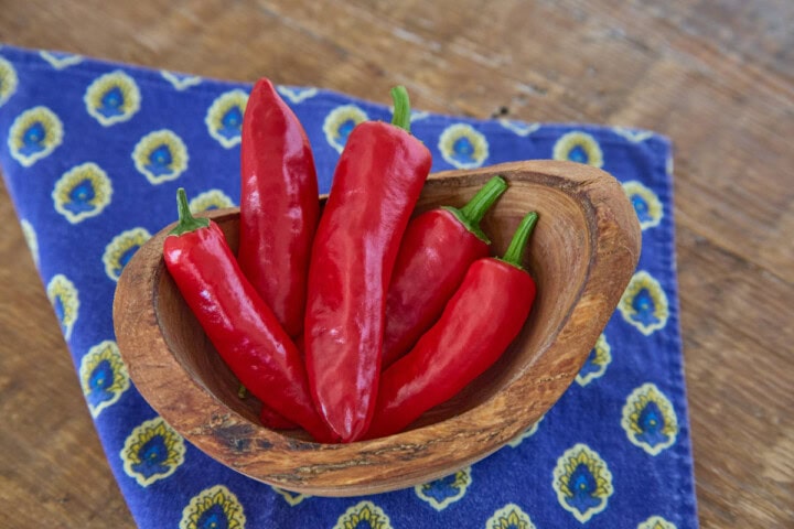 fresh piment de bresse peppers in a wooden bowl atop a napkin