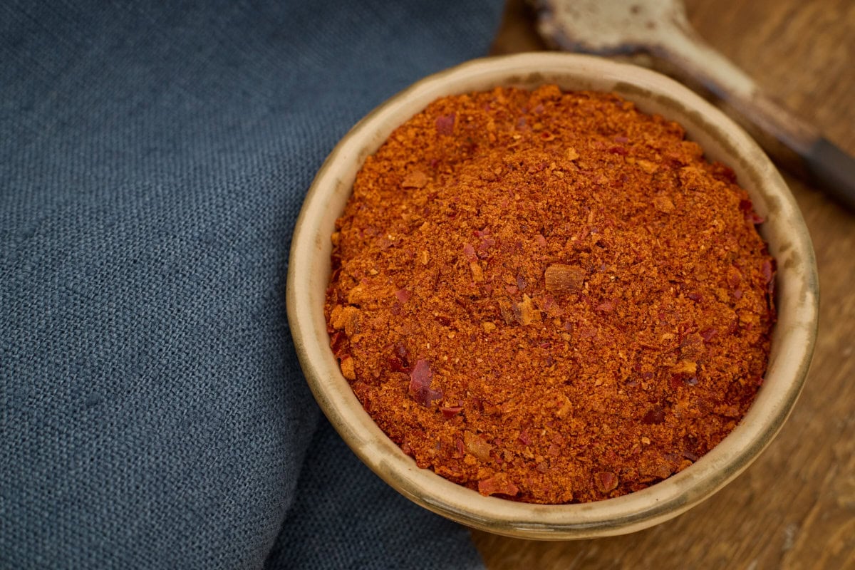 aleppo pepper powder in a bowl with a spoon in the background and a napkin alongside