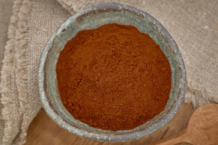 berbere pepper powder in a small bowl with a wooden spoon in the foreground and a napkin in the background