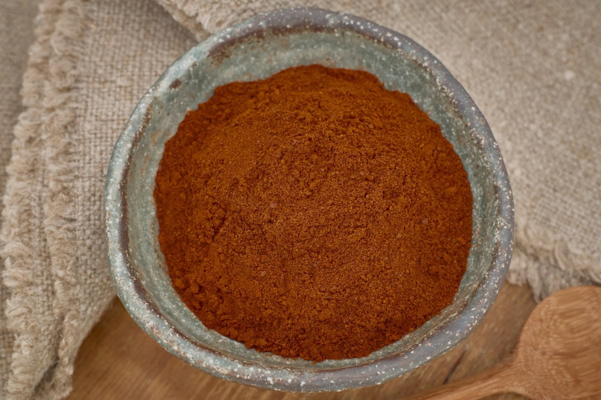 berbere pepper powder in a small bowl with a wooden spoon in the foreground and a napkin in the background