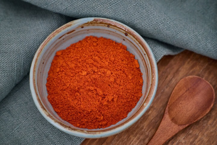 birdseye pepper powder in a small bowl with a wooden spoon in the foreground and a napkin in the background