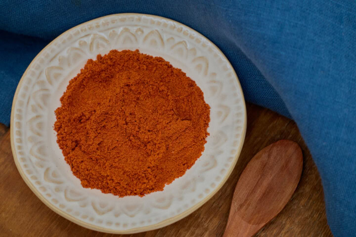 buena mulata pepper powder in a small bowl with a wooden spoon in the foreground and a napkin in the background