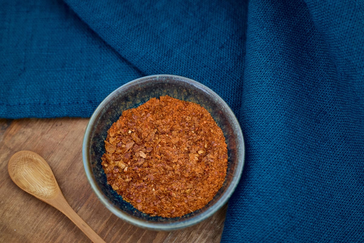 datil pepper powder in a small bowl with a wooden spoon in the foreground and a napkin in the background