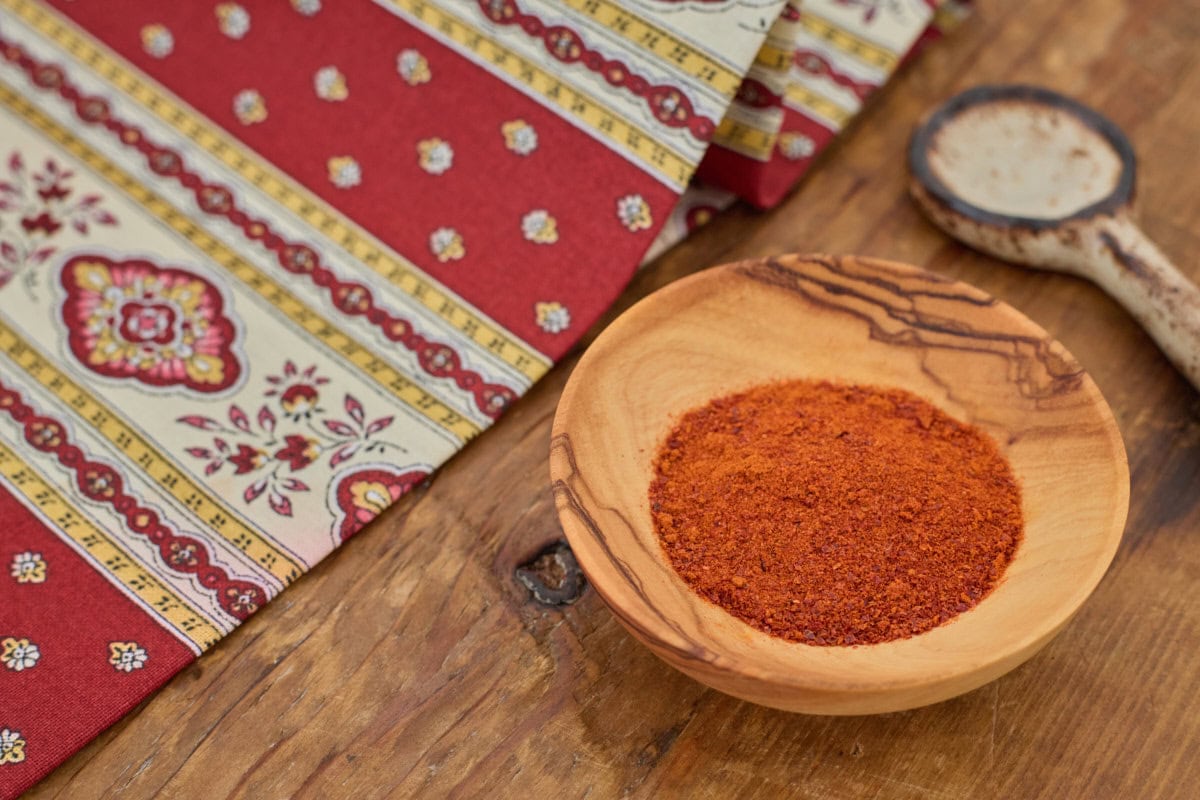 piment de bresse pepper powder in a small wooden bowl with a ceramic spoon and a napkin in the background
