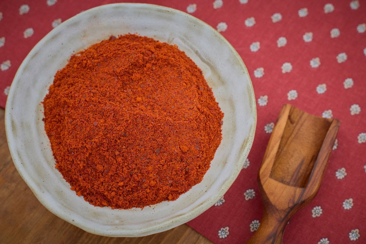 piment d'espelette pepper powder in a bowl atop a napkin with a wooden scoop alongside