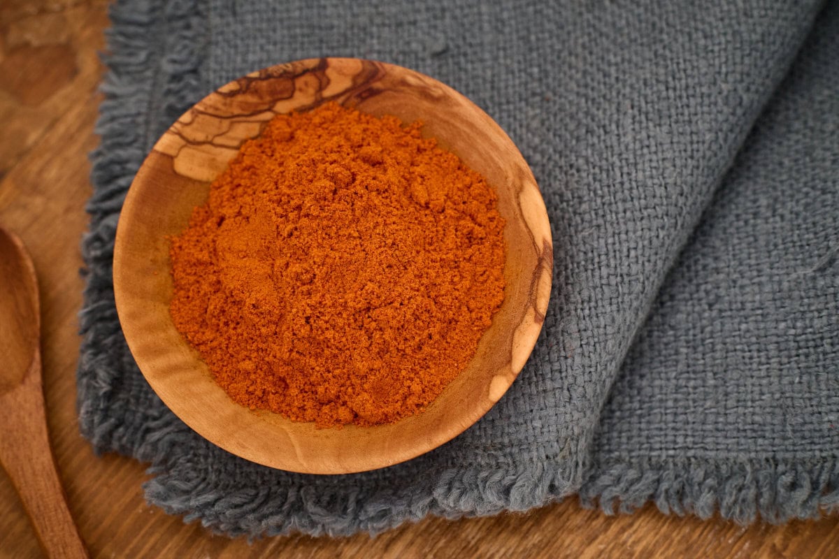 piri piri pepper powder in a small wooden bowl atop a napkin with a wooden spoon alongside