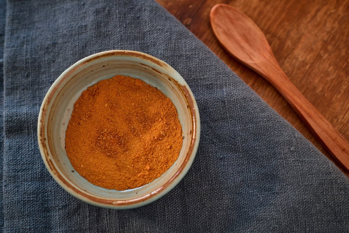 scotch bonnet pepper powder in a bowl atop a napkin with a wooden spoon in the background
