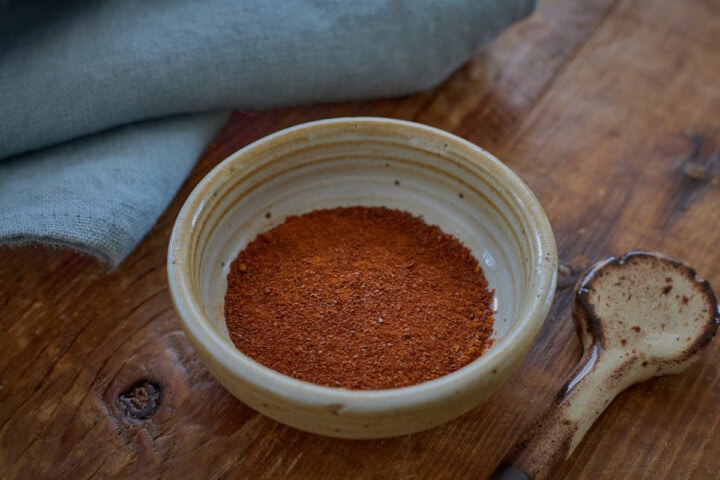 a small bowl of shisito pepper powder with a napkin and a ceramic spoon alongside